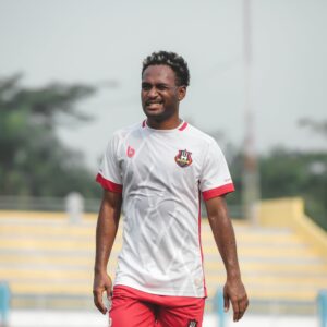 A joyful male soccer player on an outdoor field during the day, wearing a white jersey.